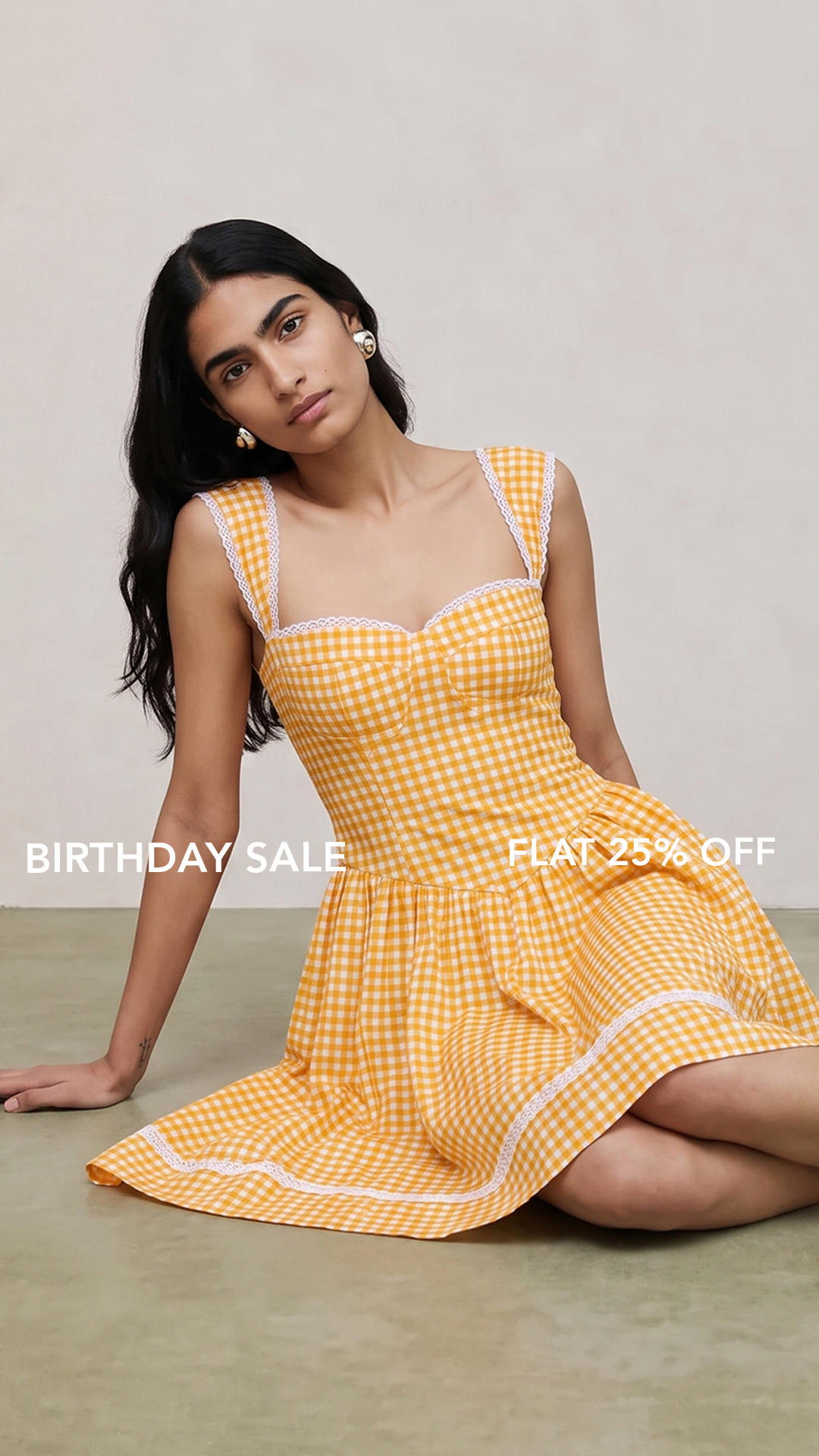A woman wearing a yellow and white gingham mini dress with white trim sits on a beige floor against a light beige wall. White text overlays read 'BIRTHDAY SALE' and 'FLAT 25% OFF'.