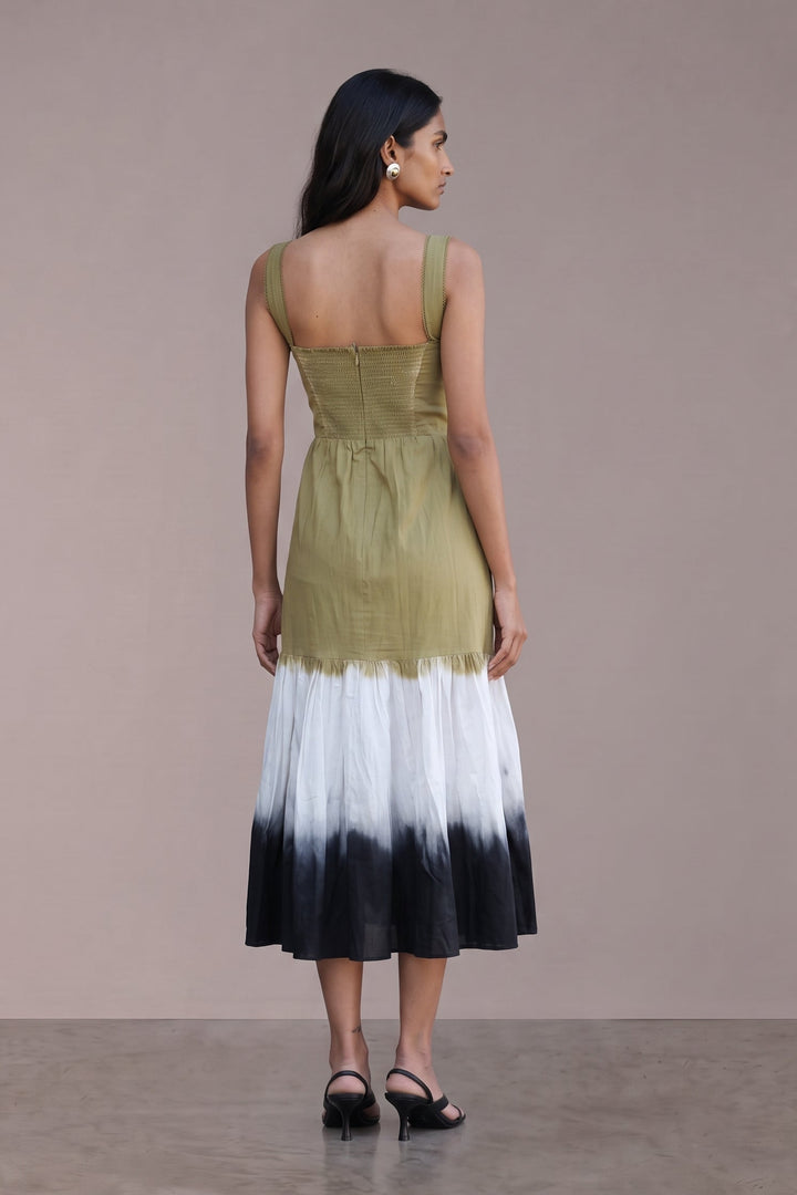 A woman stands with her back to the camera wearing a sleeveless midi dress with an olive green bodice and a white-to-black ombre skirt, set against a plain beige studio background.