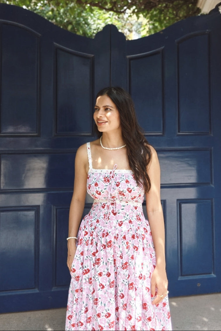 Woman in a floral dress standing in front of a large blue door with greenery above.