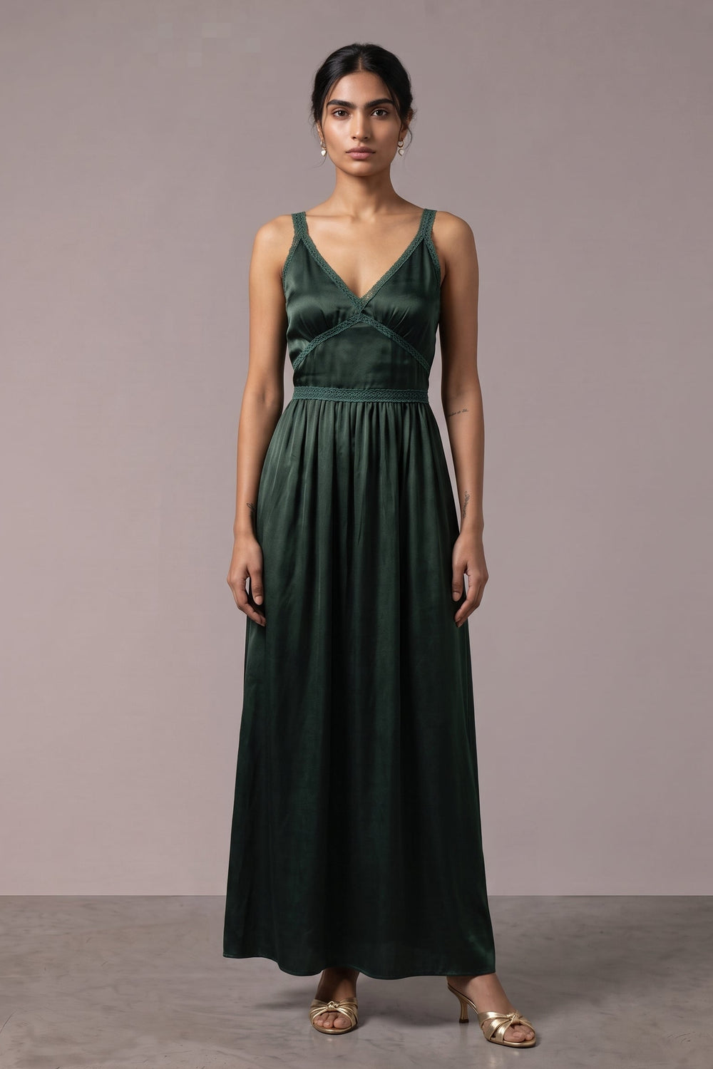 A woman modeling a dark forest green velvet sleeveless maxi dress with a V-neckline and gathered waist, standing against a neutral mauve-gray studio backdrop.