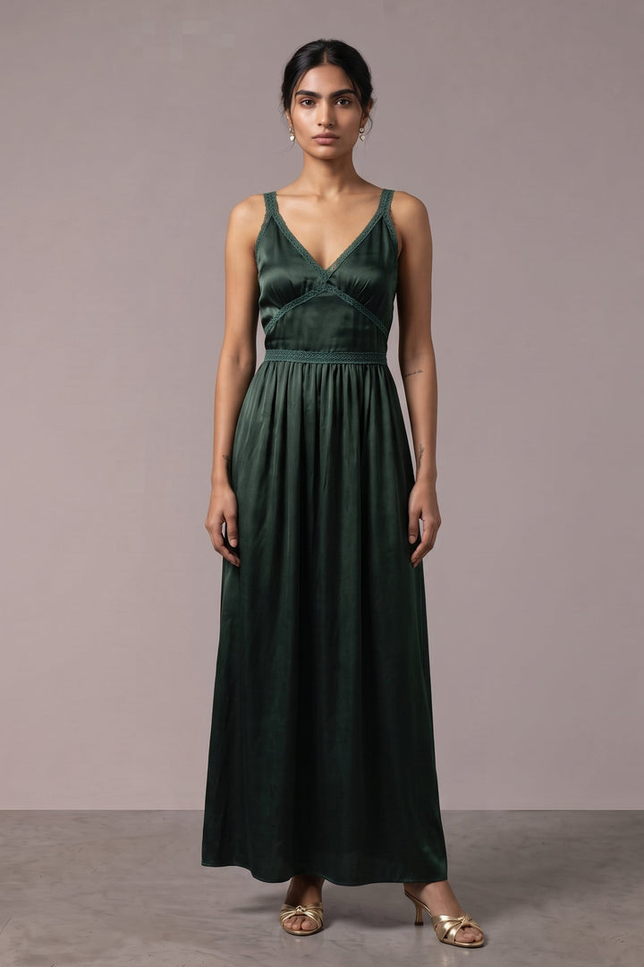 A woman modeling a dark forest green velvet sleeveless maxi dress with a V-neckline and gathered waist, standing against a neutral mauve-gray studio backdrop.