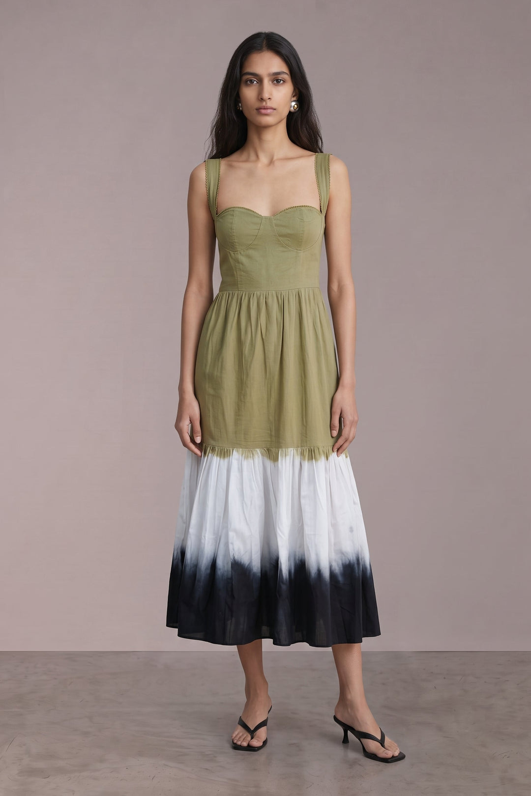 A woman modeling a sleeveless midi dress with an olive green bodice and a white-to-black ombre tie-dye skirt, standing against a solid taupe studio backdrop.