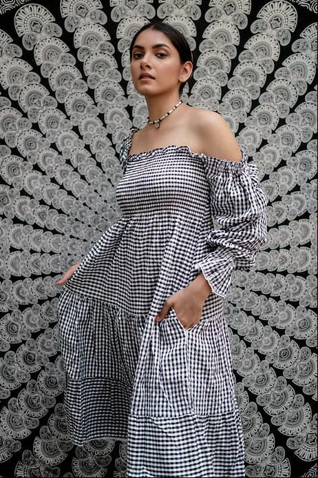 A woman wearing a gray and white checkered smock dress with puff sleeves and a multi-tiered skirt with lace trims.