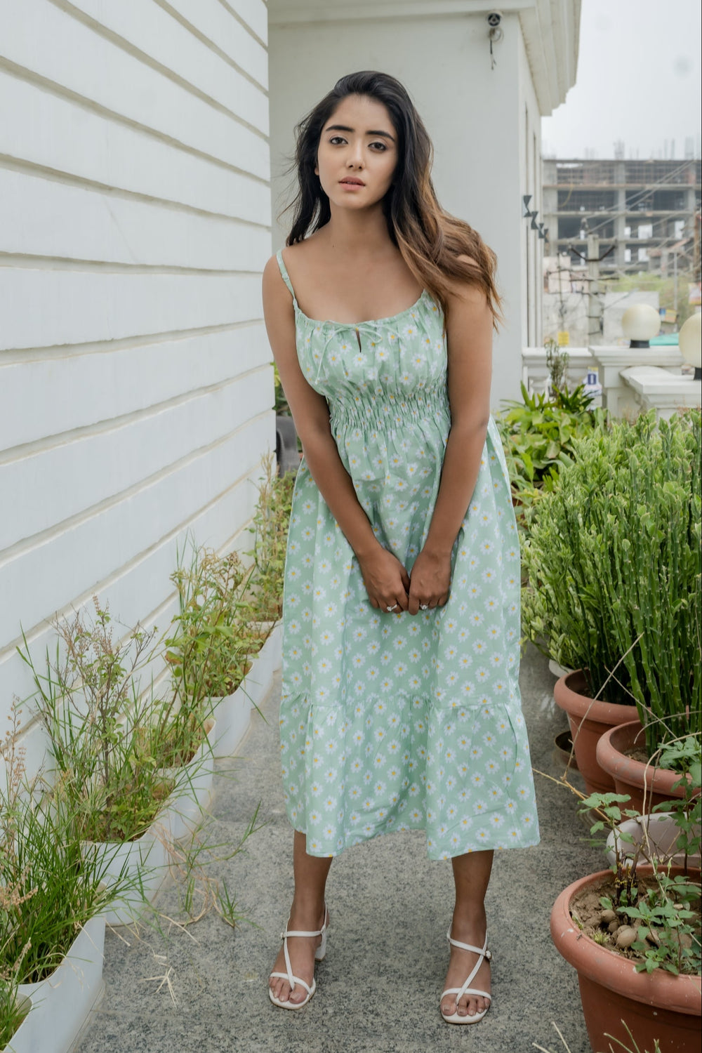 A woman standing in front of a building wearing a green midi dress with a floral pattern and a straight neckline with front keyhole detailing.