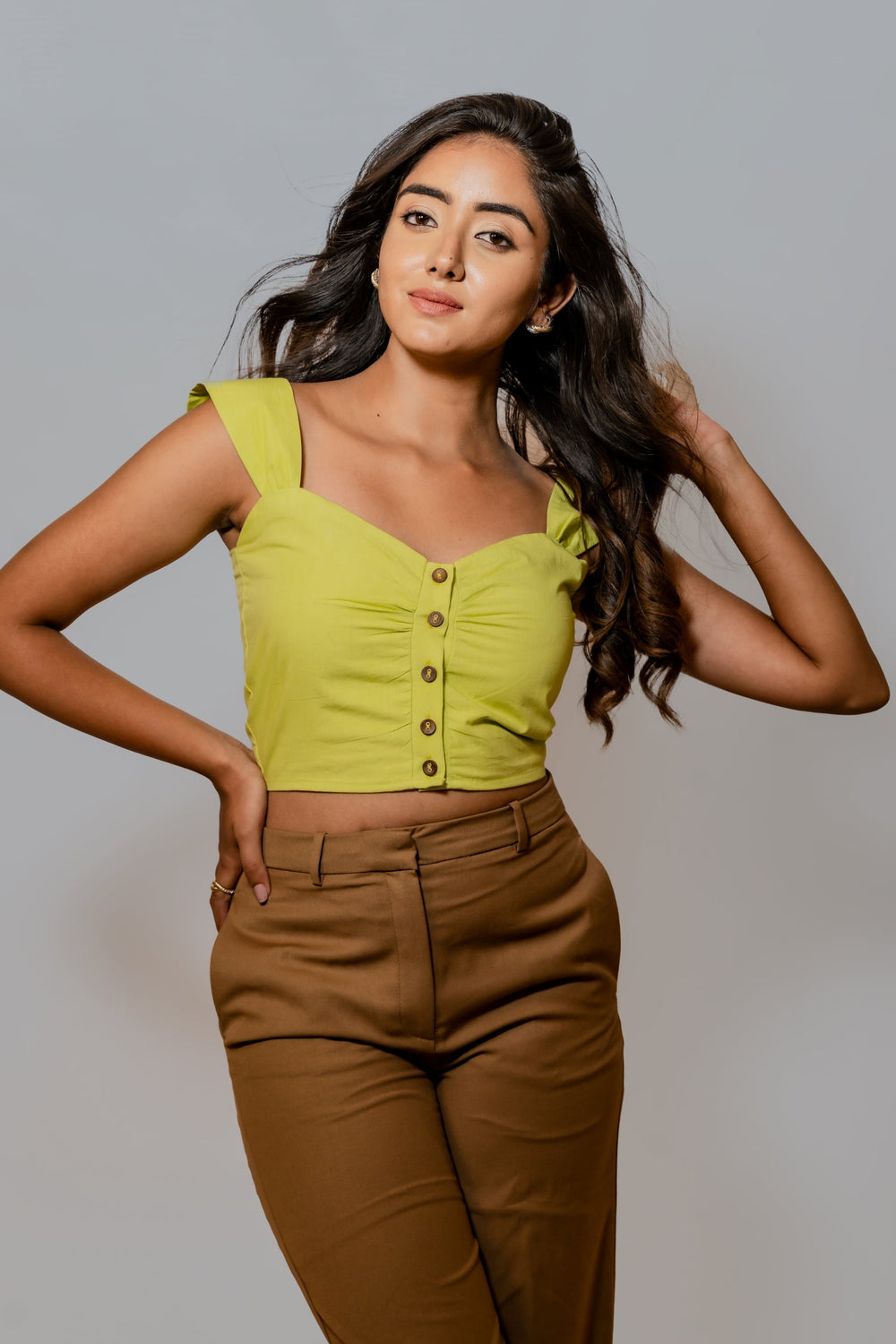 A person wearing a lime green sleeveless top with button-up front and cap sleeve detailing, paired with brown trousers.