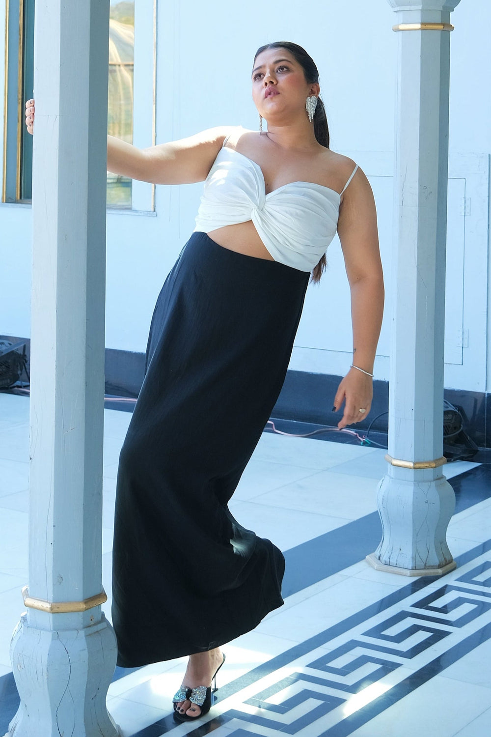 A woman standing in a black and white themed room wearing a black and white outfit with a front knot detail at the bodice and cut-out sides at the waist.