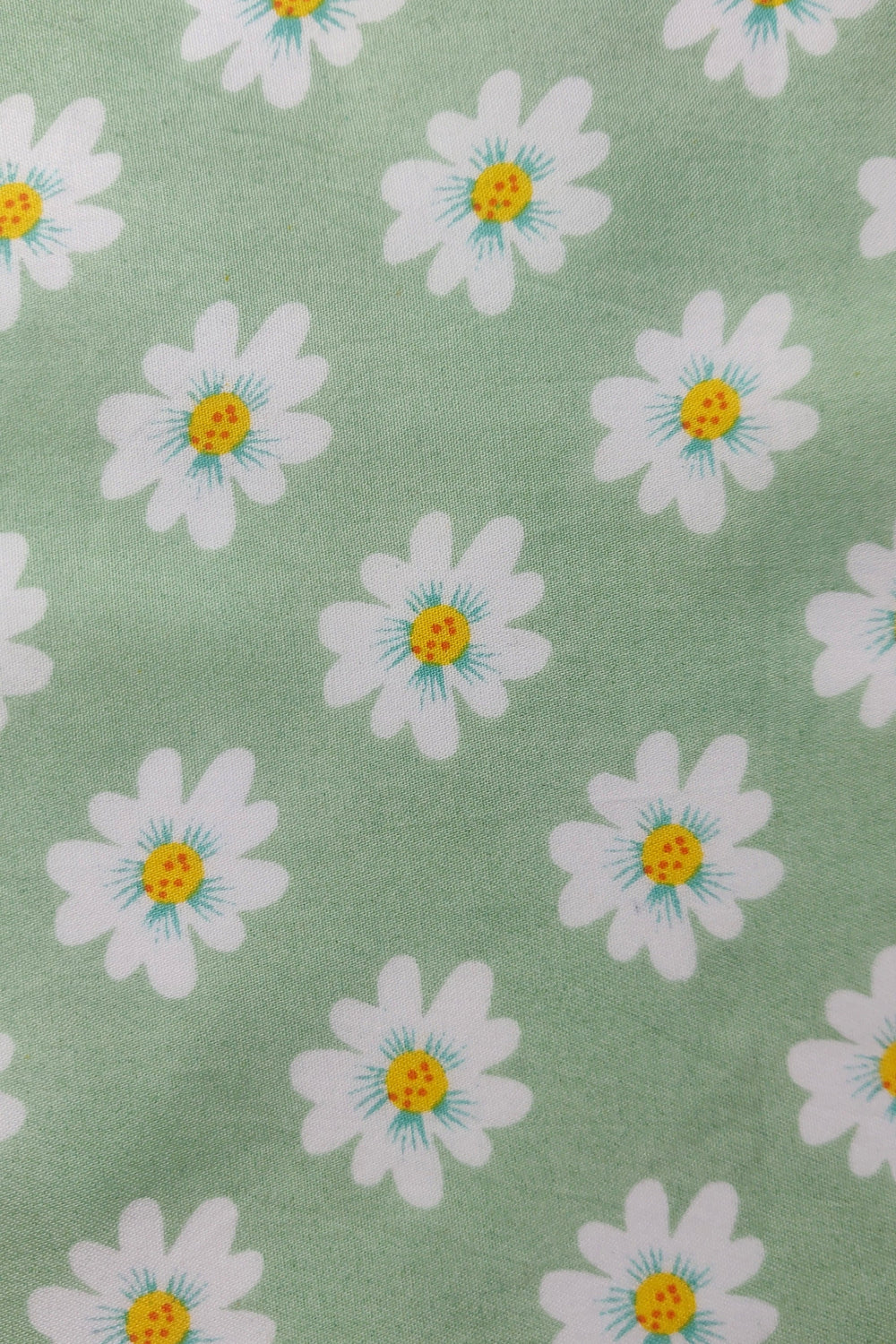 A close-up of a fabric pattern featuring white daisy flowers with yellow centers and light blue stamens on a sage green background.