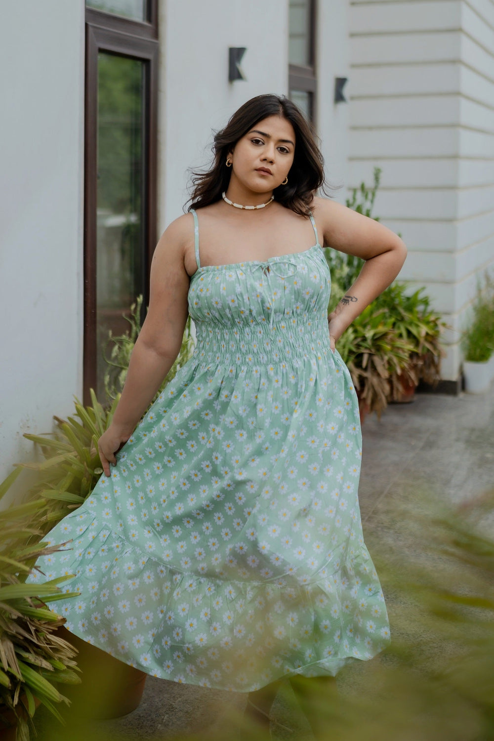 A woman standing outdoors wearing a green midi dress with a floral screen-printed motif, spaghetti straps, and a straight neckline with front keyhole detailing.